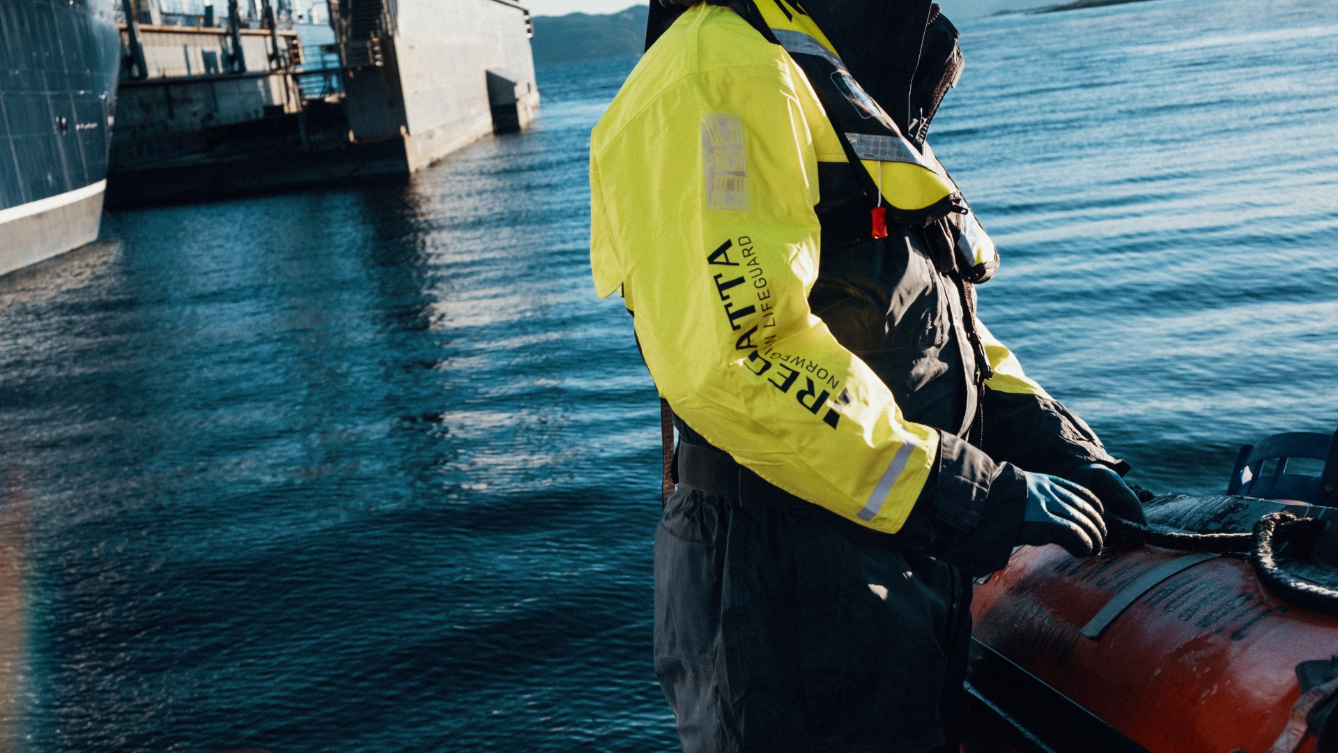 En arbeider står på en kai, iført flytedrakt og oppblåsbar redningsvest fra Regatta